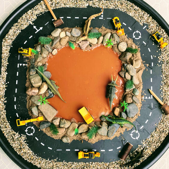 sensory play tuff tray inviting children to play with roads, toy dinosaurs, toy diggers, sand, rocks & muddy water